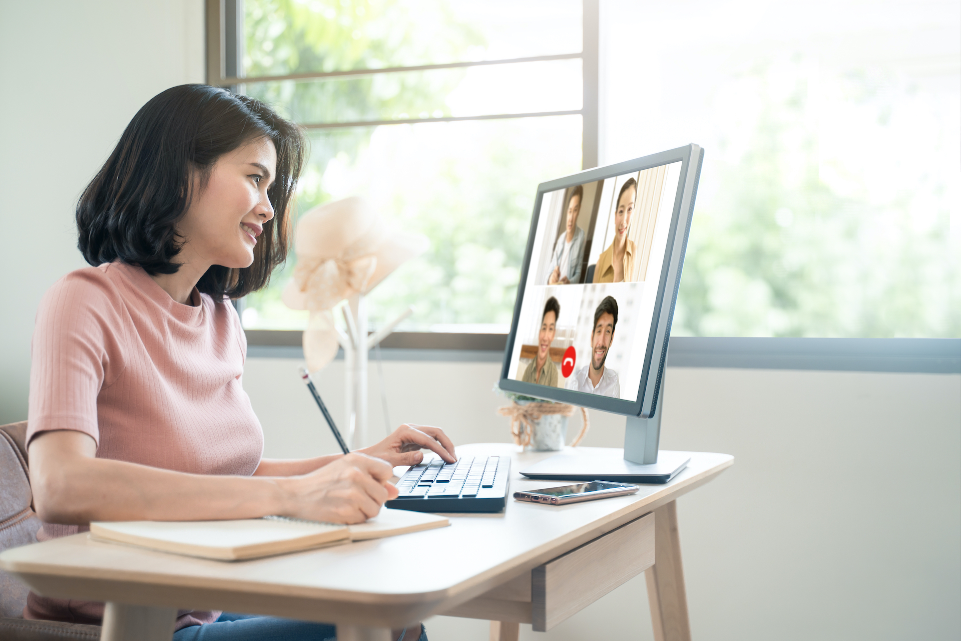 Asian woman professional sitting at a desk, pencil in hand, having a video call meeting on a computer