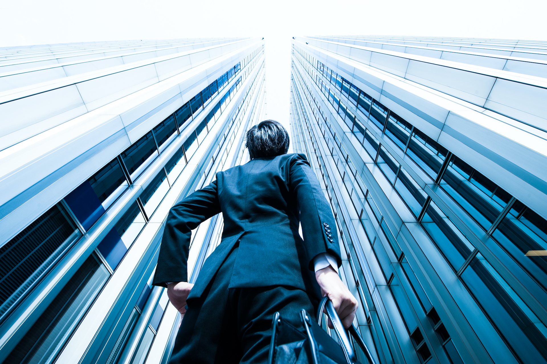 Man in suit holding a briefcase and looking up at a skyscraper