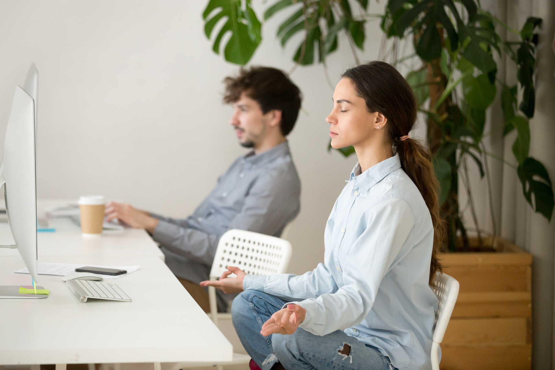 Man and woman in shirts and jeans meditating at a work desk in front of a computer screen