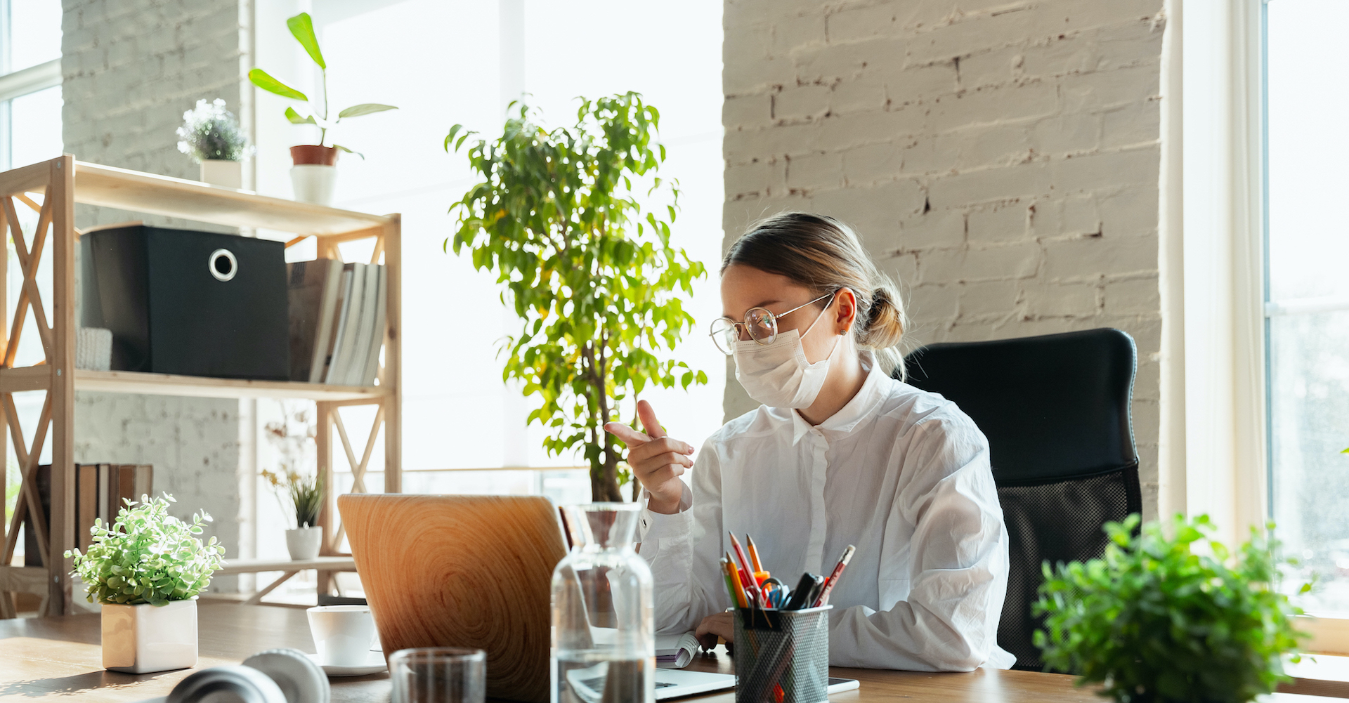 Woman in white shirt pointing at laptop, working from home at a desk with stationery, file cabinet on the side