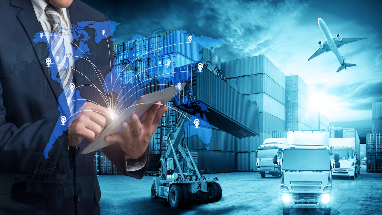 Man in suit with electronic pad standing against a supply chain backdrop with world map in the foreground