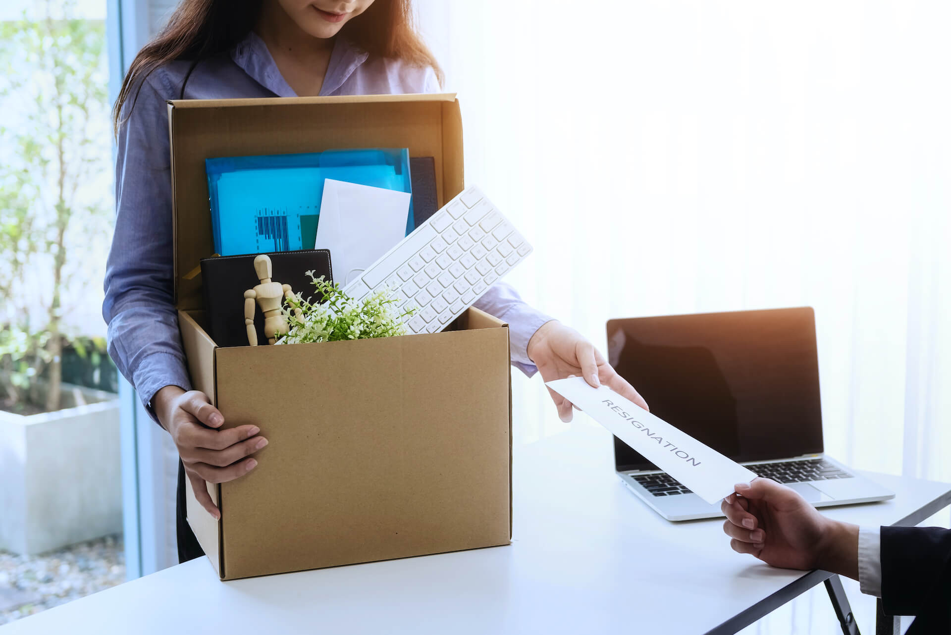 Woman carrying belongings in cardboard box hands in her resignation